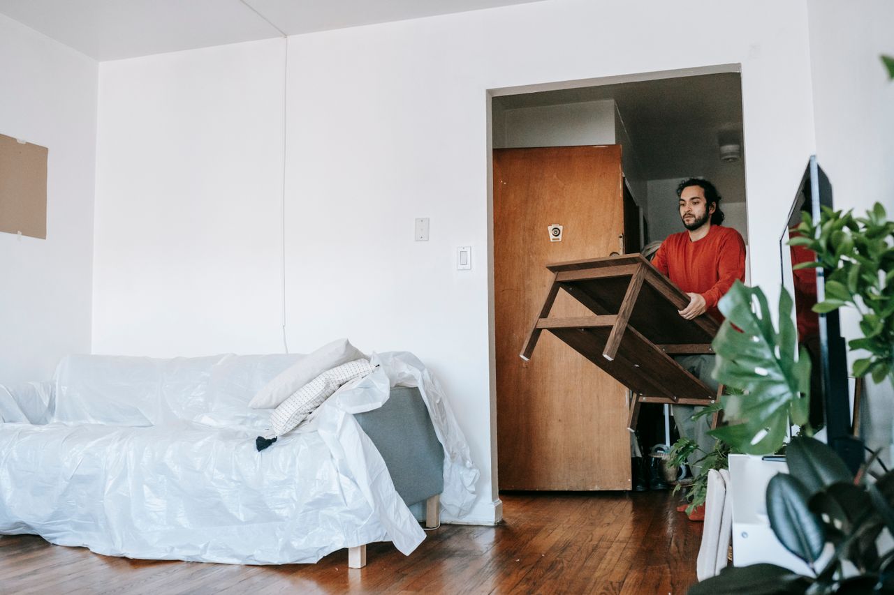 Man holding a wooden table during relocation in a contemporary apartment.